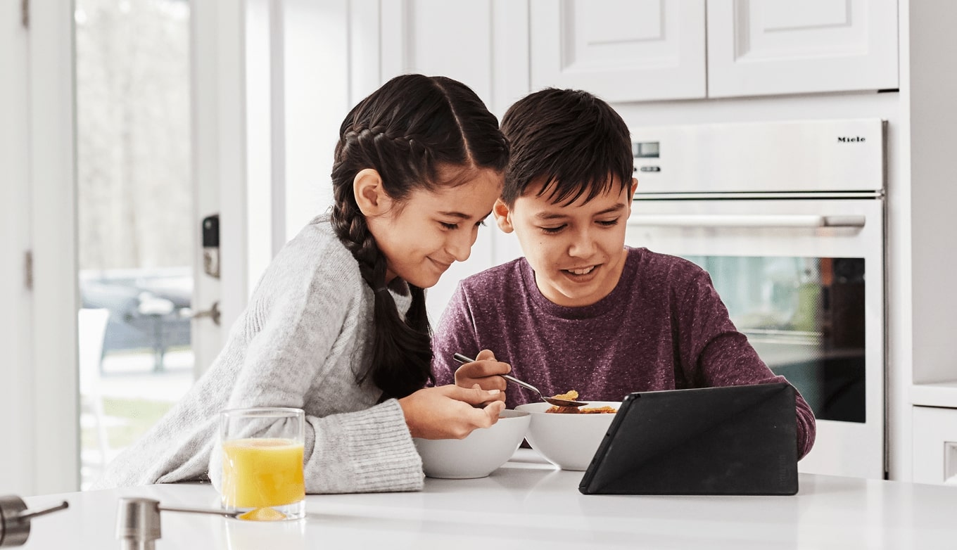 Kids in kitchen, eating cereal watching a tablet