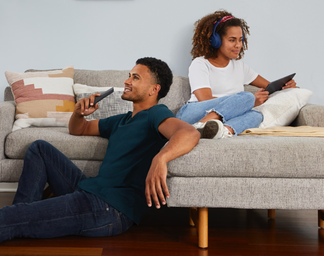 Man speaking into remote and woman using tablet on couch