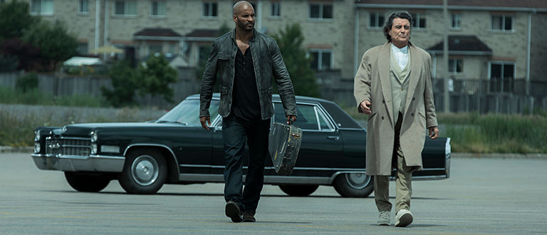 Two men walking in front of a car from the Starz show American Gods